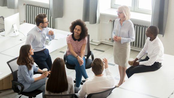 Group of office workers gathered around talking and smiling