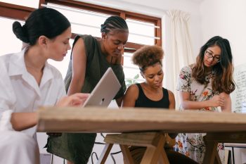 Group of 4 employees gather around table with laptop having a meeting