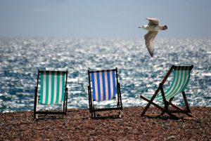 Three empty deck chairs on a beach with blue sky and the sea in the background