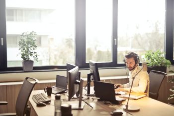 Man with large headphones sits at office desk with two PC screens