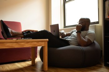 Man relaxed working from home on laptop, sat on bean bag with feet up on coffee table