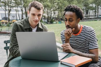 two men sat outdoors looking at laptop screen