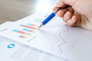 Two pages showing graphs and data charts with person holding blue pen