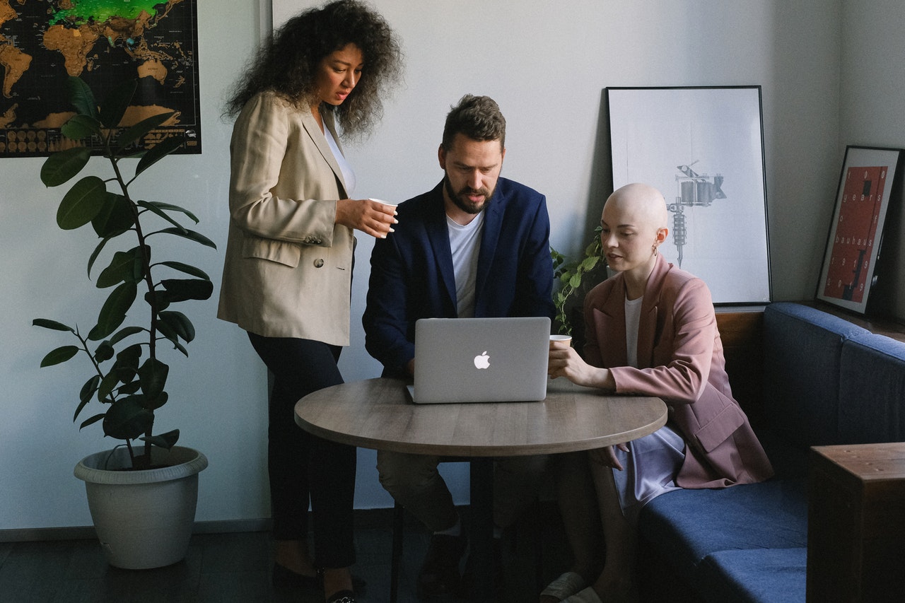 3 people in a modern trendy office gathered around looking at a laptop screen