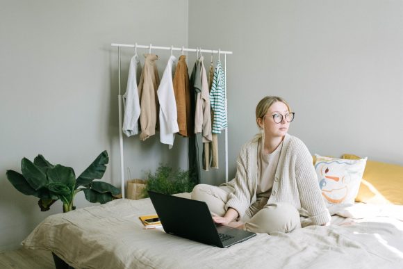 woman sitting on bed with laptop in front of her and looking off into the distance