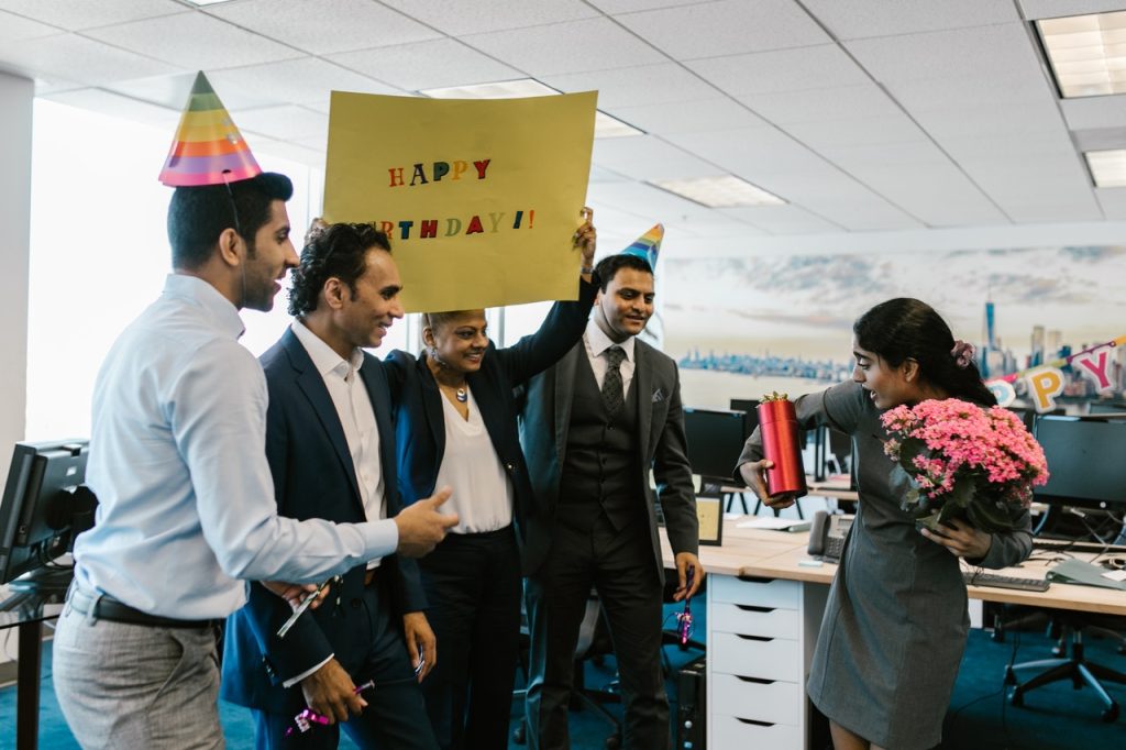 group of office workers smiling with happy birthday signs and party hats