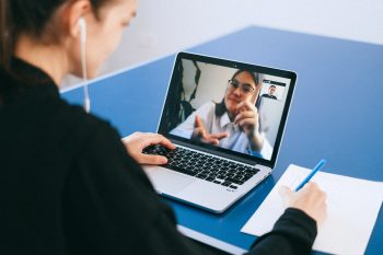 woman with earphones sat at desk video calling colleague
