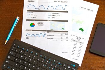 documents on a table showing charts, tables and web analytics. next to a keyboard and a pen