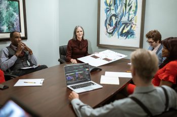 5 professionals sat around a conference table with laptops in front of them
