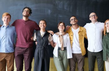 7 employees standing arm in arm smiling at camera in front of large chalkboard