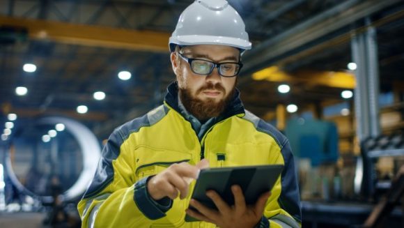 worker checks ipad wearing bright clothing and a hard hat