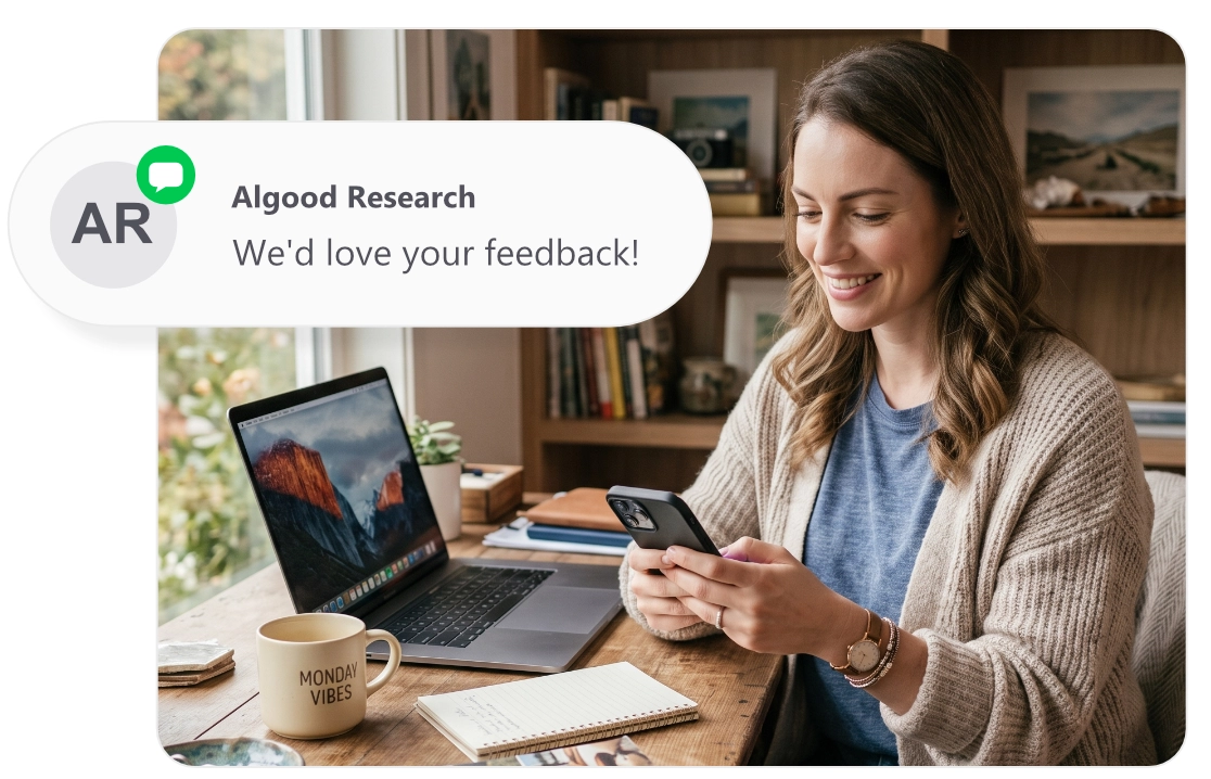 A woman working at home receives an SMS text message on her smartphone. The message reads "Algood Research - We'd love your feedback!"